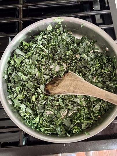 Chopped kale, carrot tops, and basil wilting in a heavy bottomed saucepan with shallots and garlic