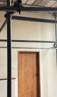 An empty hallway, with a closed wooden door in the middle of a blank beige wall. Scaffolding is visible in the space.