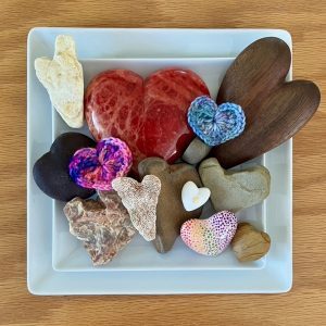 A blue ceramic bowl with logs to different heart shapes some red, others wooden, some in stone.
