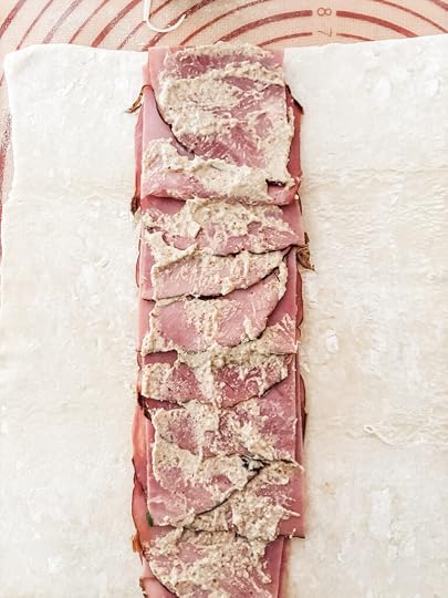 Thin-sliced deli ham layered down the center of a rolled puff pastry sheet with mustard and shredded Swiss cheese