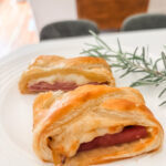 Sliced ham and cheese strudel on a white serving board showing flaky golden pastry and melted Swiss cheese filling