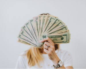 Woman whose face is obscurred by fanned out $20 bills