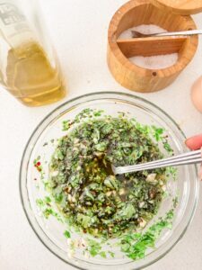 A glass jar of fresh chimichurri sauce with chopped parsley, oregano, minced garlic, and red pepper flakes in olive oil