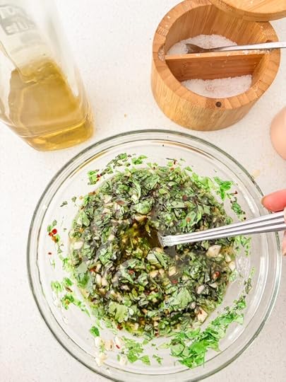 A glass jar of fresh chimichurri sauce with chopped parsley, oregano, minced garlic, and red pepper flakes in olive oil
