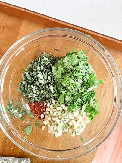 Freshly chopped parsley, garlic and oregano in a glass bowl on a wooden cutting board