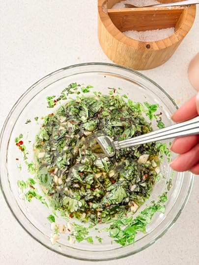 A glass bowl with the prepared chimichurri, being stirred with a fork