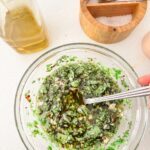 A glass jar of fresh chimichurri sauce with chopped parsley, oregano, minced garlic, and red pepper flakes in olive oil