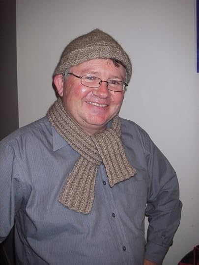 Russell smiling and wearing a scarf and hat knit from a warm grey fuzzy yarn.