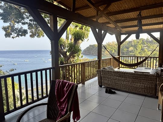 A serene balcony view overlooking a calm sea with boats, featuring a hammock, a wicker sofa, and tropical greenery.