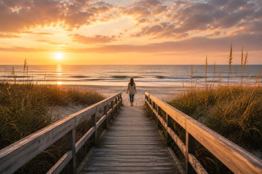 Wooden boardwalk through dune grass with woman walking toward beach at sunrise