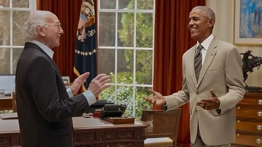 Larry David and Barack Obama smiling and gesturing during a conversation in the Oval Office.