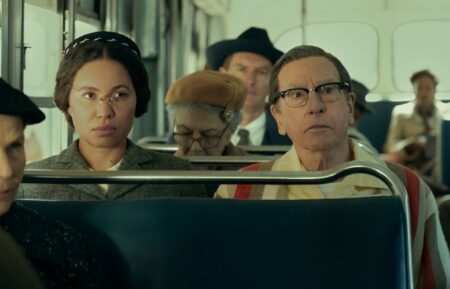 A diverse group of people sitting on a bus, with a focus on a woman with glasses and a man looking intently ahead, illustrating a moment of tension or contemplation.