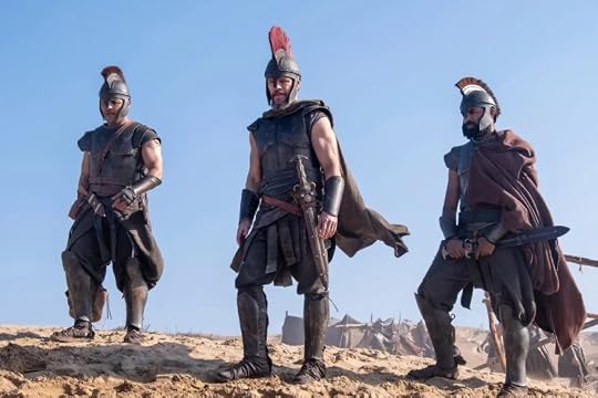 Three armored warriors standing on sandy terrain, wearing helmets and capes, with weapons visible at their sides.