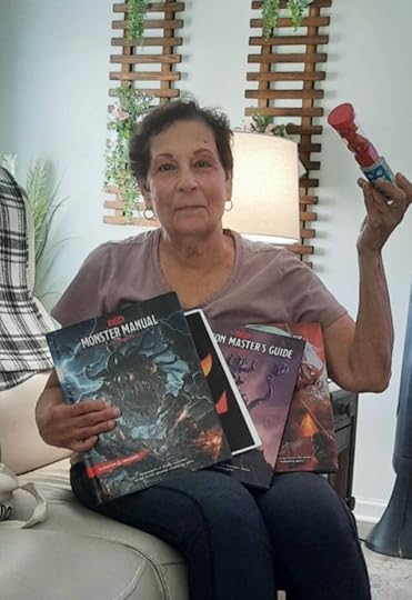 A woman sitting on a couch holds multiple role-playing game books, including a 'Monster Manual' and 'Dungeon Master's Guide,' while showing a colorful toy in her other hand.