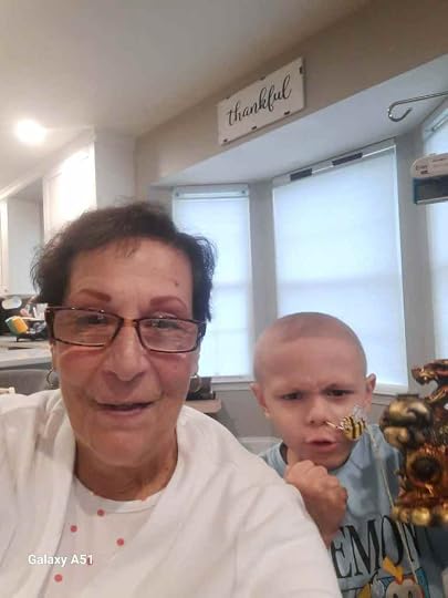 A woman and a young boy smiling together for a selfie, with the boy holding a small golden statue. The background shows a well-lit room with windows and a 'thankful' sign.