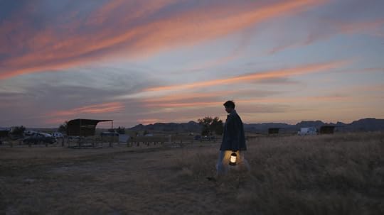 A person walking in a grassy field at dusk, carrying a lantern, with colorful sunset clouds in the background.