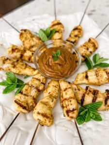 The finished Asian Chicken Skewers with Peanut Dipping Sauce on a plate with green garnish