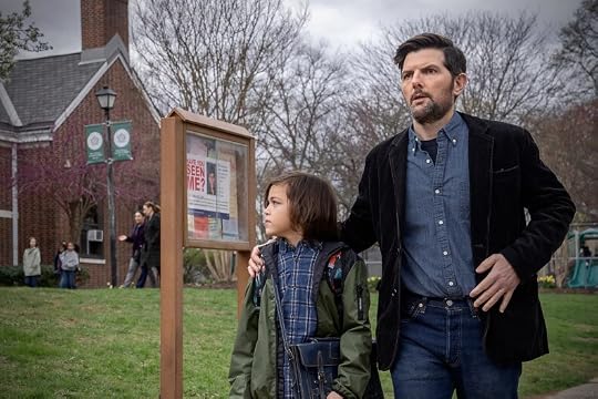 A man and a child standing outside, looking at a notice board with a missing person poster, in a park-like setting.