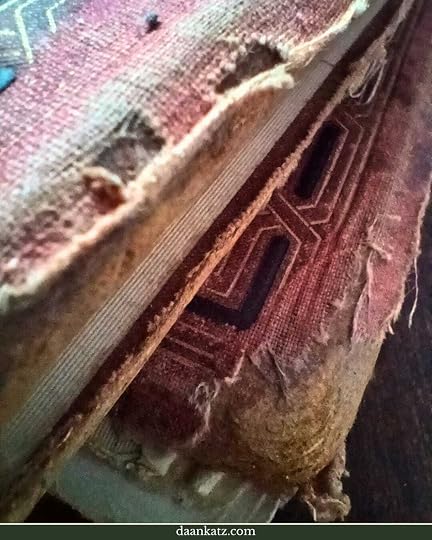 Close-up of a worn, frayed book cover showing exposed fabric and visible spine, with part of an embossed geometric pattern.