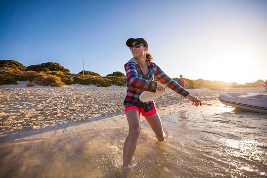 Woman standing on a beach at the edge of the water getting ready to throw a frisbee.