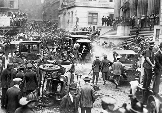 A historical black and white image depicting a chaotic street scene with numerous people gathered around overturned cars, with some officers present, and a crowd in the background.