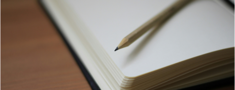 Sharpened wooden pencil resting on an open blank notebook with cream-colored pages.