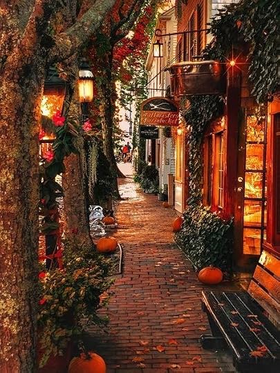 This may contain: an alley way with pumpkins on the ground and lights hanging from buildings in the background