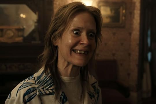 A close-up of a woman with wild hair and an exaggerated facial expression, showcasing prominently missing teeth and wide eyes, set in a dimly lit room with vintage decor.