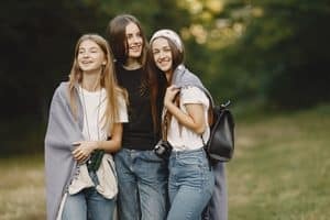 three young teenage girls stand in a grassy field together.