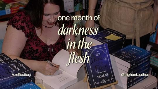 MG Hunt smiling signing copies of Darkness in the Flesh. Yellow text on top of the image reads: One month of Darkness in the Flesh.