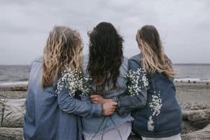 Three women looking out at water holding flowers.