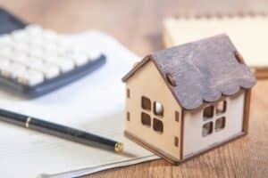 Small wooden house on top of papers with a calculator and pen
