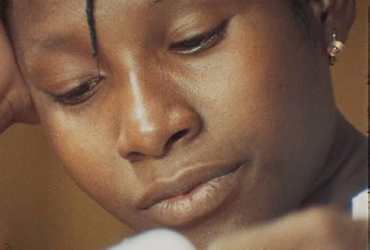 Close-up still from Den Muso showing Tenin looking downward with a subdued expression, her head resting against one hand and a thin braid falling across her forehead.
