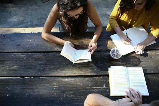 Two people reading books and writing in a notebook at a wooden picnic table