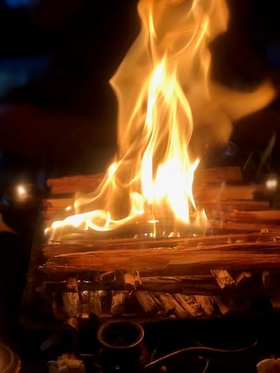 A single tall flame rising from a fire pit in a darkened room, embers glowing at its base
